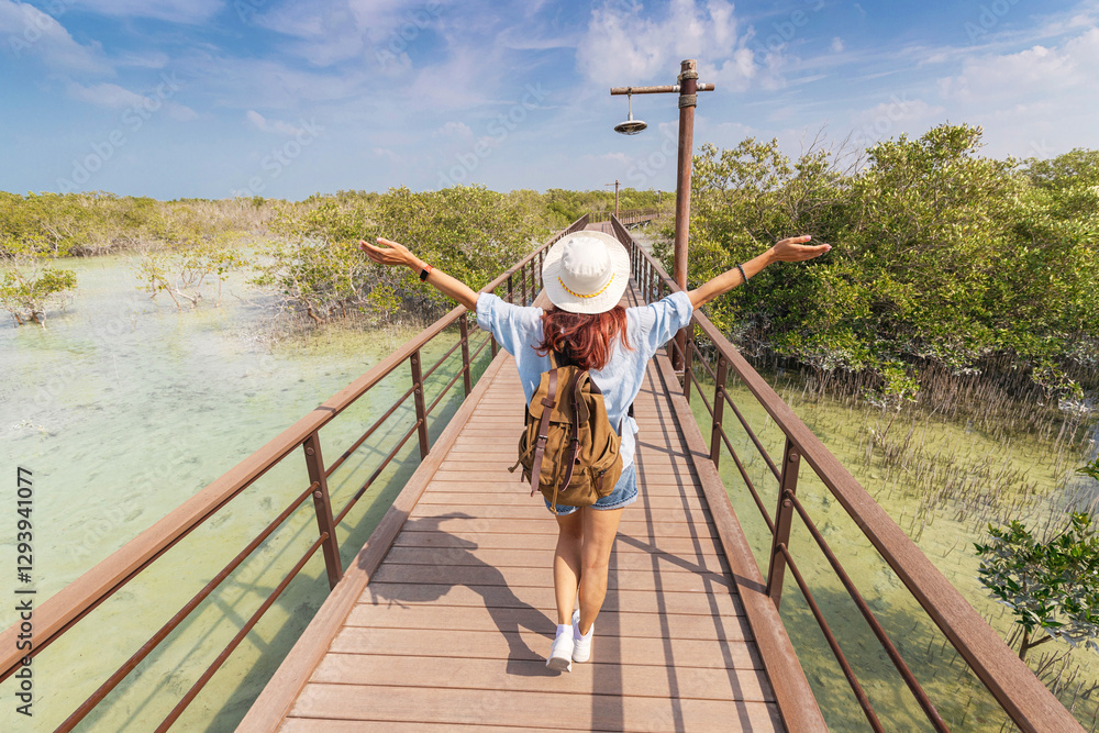Woman with backpack joyfully walks along a wooden boardwalk through a serene mangrove forest park, embracing adventure