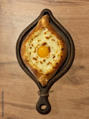 Georgian dish Adjarski Khachapuri on a dark wood serving board on a wooden table photo