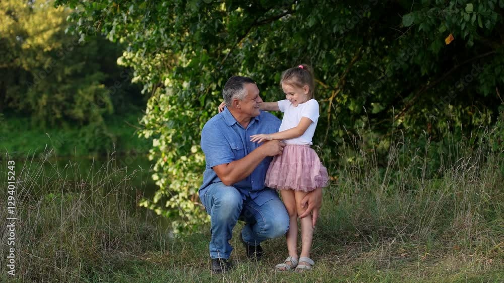 Middle aged dad squatting gently tickling and hugging cute girl creating warm, tender moment together outdoors during walk in park spending time together. Trusting father and daughter relationship Middle aged dad squatting gently tickling and hugging cute girl creating warm, tender moment together outdoors during walk in park spending time together. Trusting father and daughter relationship