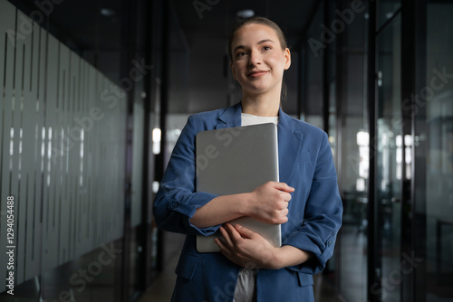 Принти на полотні Confident young student, intern, or aspiring professional standing in a modern office hallway, holding a laptop