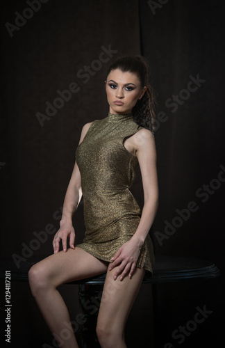 Obraz na płótnie Portrait of a beautiful young brunette girl in a gold short dress on a dark background. w salonie