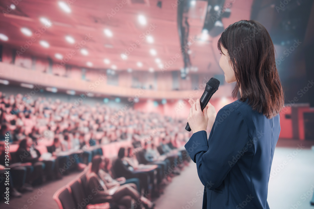 大勢の聴衆が集まるホールで司会をする若い女性 大勢の聴衆が集まるホールで司会をする若い女性