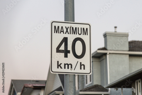 A close-up of a speed limit sign displaying a maximum of 40 km per hour, located in a suburban residential neighborhood with houses in the background. photo