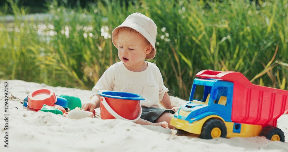 Child plays with a shovel on the beach near the water, pouring sand into a bucket, surrounded by toys, focused on the task at hand. Child plays with a shovel on the beach near the water, pouring sand into a bucket, surrounded by toys, focused on the task at hand.