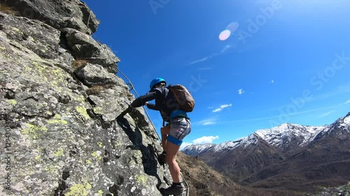 A mountaineer climbs a near-vertical rock wall, their muscles tense as they navigate the exposed route high above the valley floor.