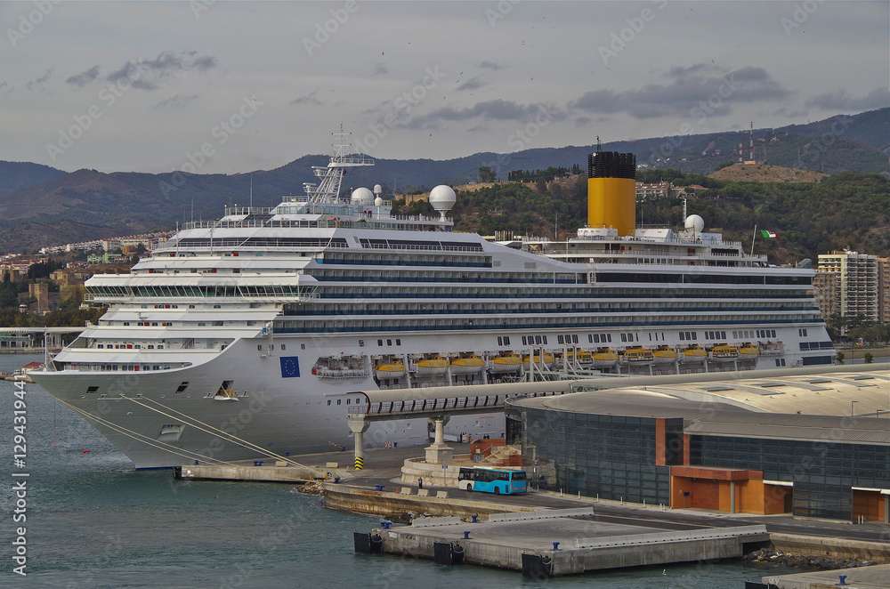 Naklejka premium Modern mega cruiseship cruise ship liner Fortuna docked in Malaga, Spain with beach and coast line beautiful nature landscape scenery and city skyline during Mediterranean cruising