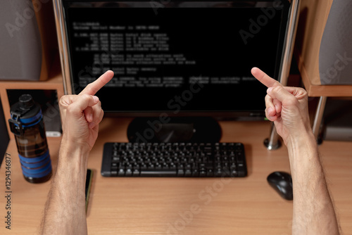 Angry man showing middle fingers to computer screen with system error warning. Man facing monitor, system error message displayed, rear view