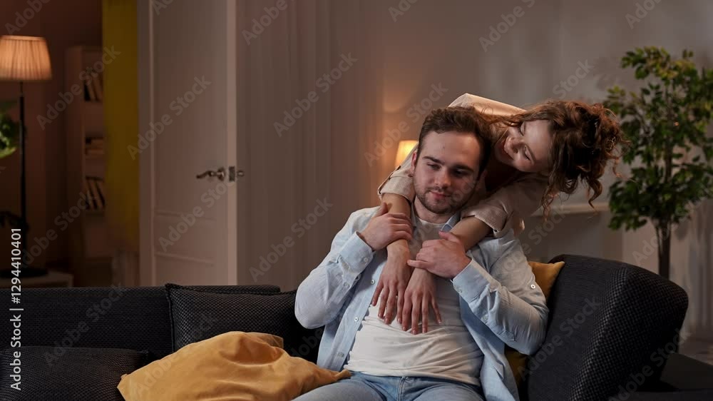Lovely couple relaxing on couch at home, man and woman in the room watching tv, woman hugging man from behind, couple talking and cuddling. Slow motion. Lovely couple relaxing on couch at home, man and woman in the room watching tv, woman hugging man from behind, couple talking and cuddling. Slow motion.