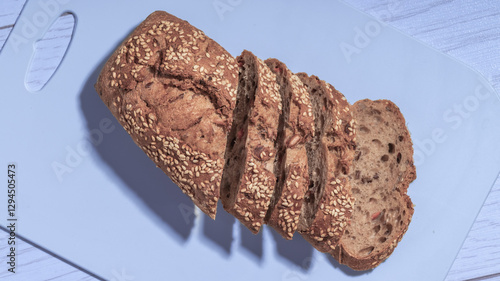 Bild auf Leinwand A loaf of whole grain bread with sesame seeds, partially sliced, placed on a light blue cutting board