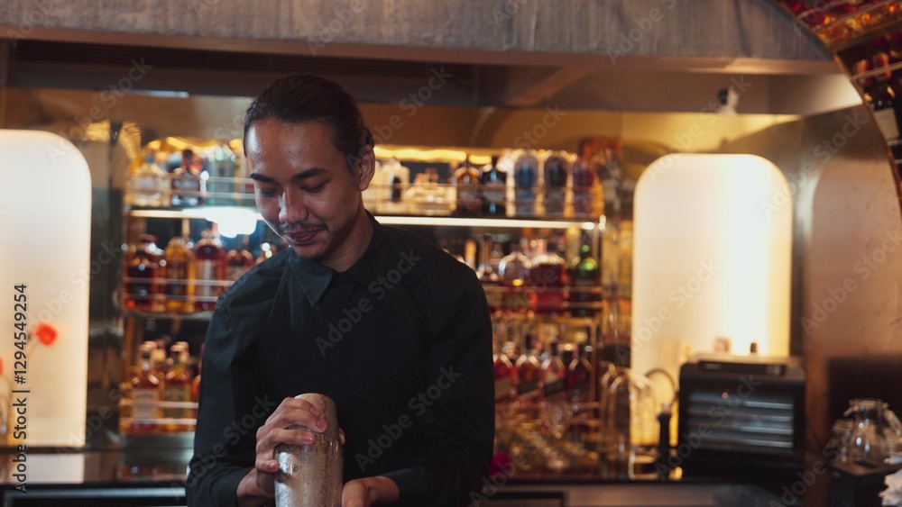 Obraz premium Asian smart bartender shaking mixed cocktail preparing to serve at luxurious counter preparation, making special drink looking at camera fronted view. Special refresh drink nightlife luxury. Vinosity.