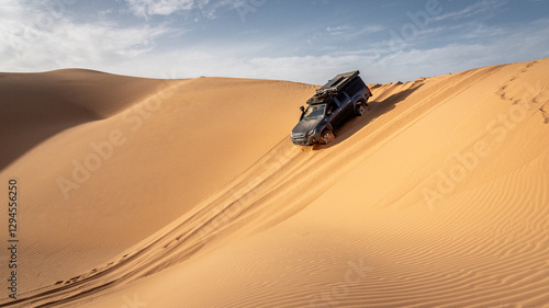 A 4x4 camper equipped with a roof tent crosses a sand dune of the Admer erg in the heart of the Algerian Sahara desert
