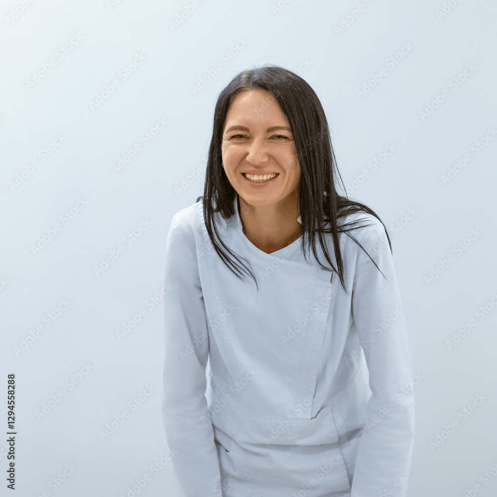 A female massage therapist in a light blue uniform smiling and leaning forward slightly in a friendly manner. A female massage therapist in a light blue uniform smiling and leaning forward slightly in a friendly manner.