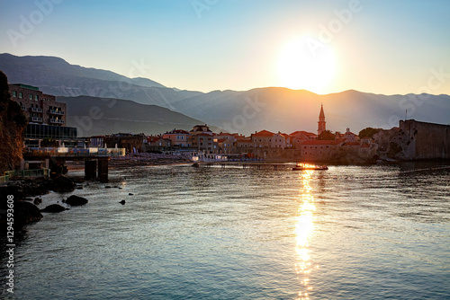 Sunset glows over a tranquil bay with the charming old town of Budva set against a backdrop of majestic mountains.