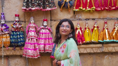 Portrait of young Indian woman looking at puppets hanging on wall of Jaisalmer local market, Rajasthan, India. Rajasthani Kathputli wearing colorful traditional Rajasthani clothes. photo