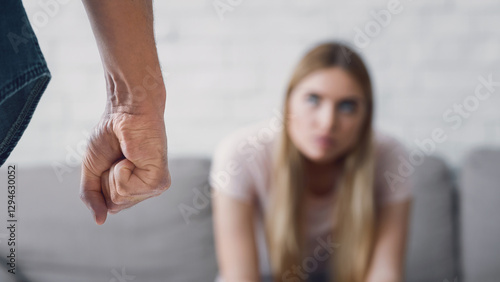 Free Download Fear and problems in family. Angry man with fist close up, and sad woman sits at sofa in living room interior - GFXLoad
