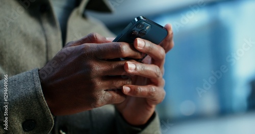 A man of African American appearance uses a mobile phone, standing near a building in which lamps shine in the windows. Close-up of male hands with a phone, no face. Video in 4k, red komodo