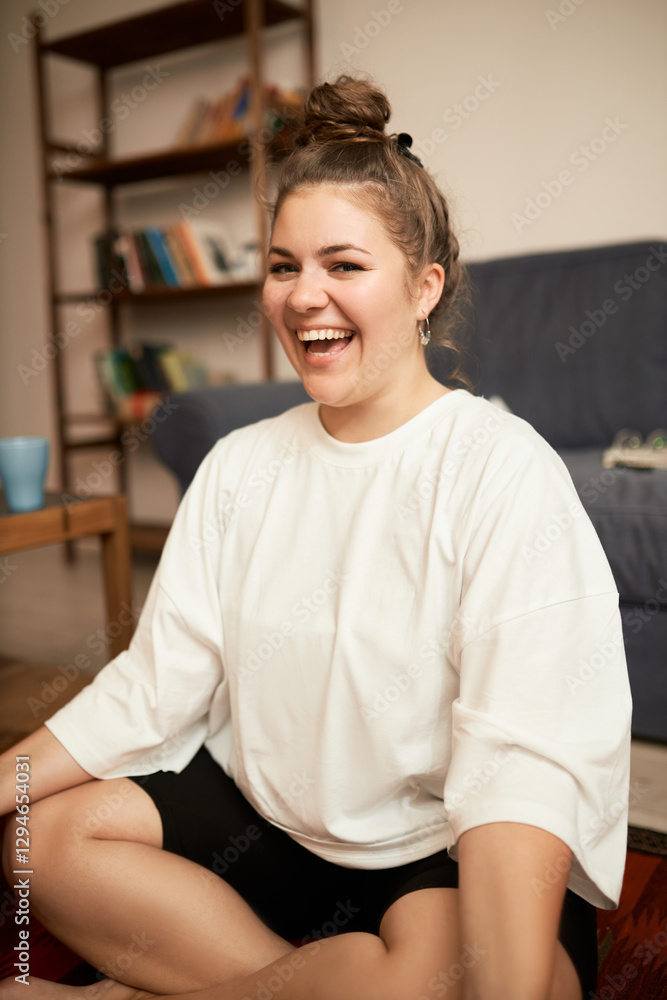 Crop shot of happy cheerful plus size female having fun after finishing her yoga practice at home, laughing feeling relaxed and energized, looking at camera sitting in lotus posture Crop shot of happy cheerful plus size female having fun after finishing her yoga practice at home, laughing feeling relaxed and energized, looking at camera sitting in lotus posture