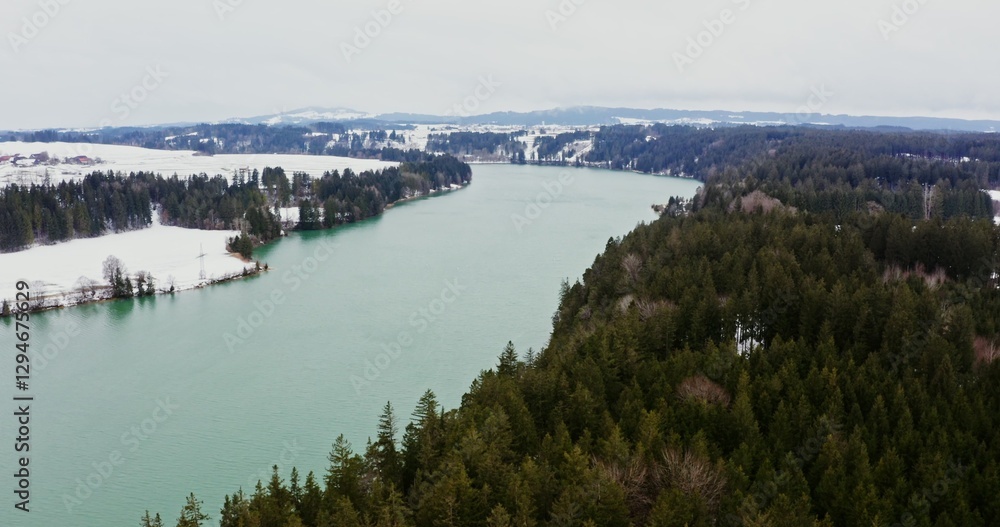 Fototapeta premium Video filming from a bird's eye view, from a drone . View of a wide river flowing through forests and snowy fields. Village on the banks of the river, drone video