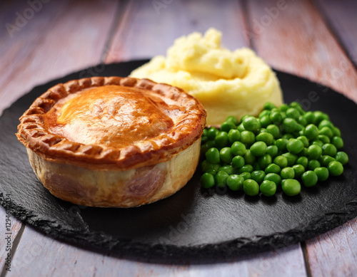 Fotografie Traditional British pie served on a slate plate with potato mash and peas