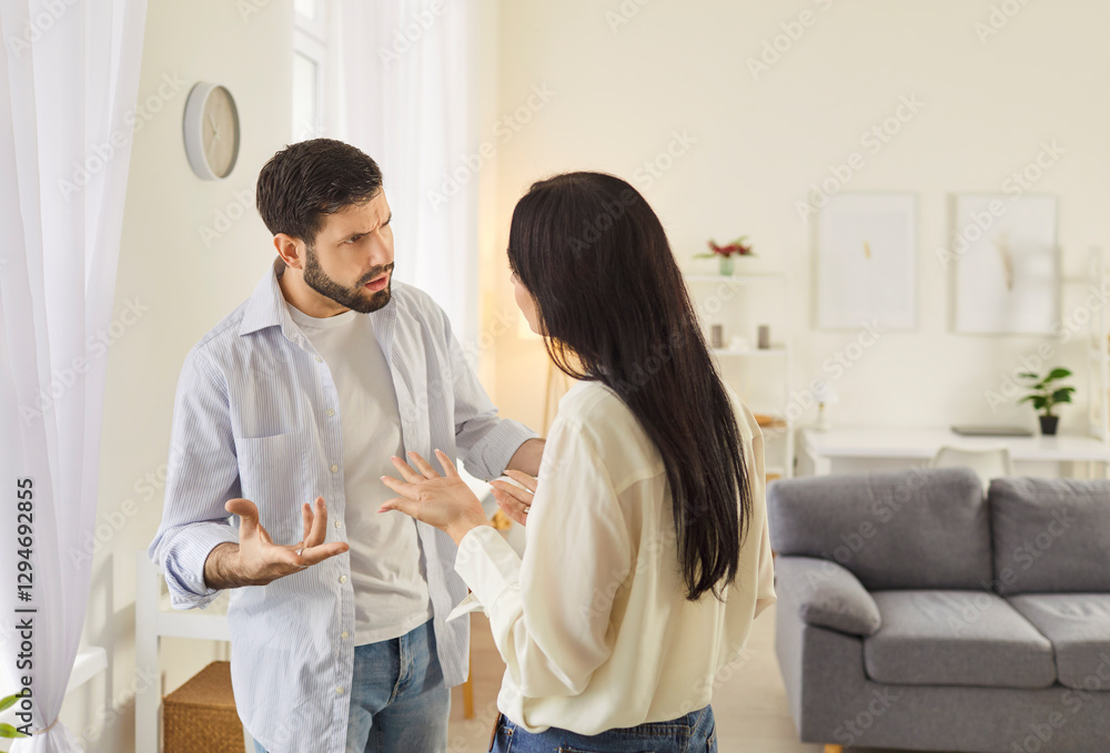 Obraz premium Young family couple arguing in living room, showing signs of disagreement. Angry husband and wife quarreling, expressing frustration and disappointment. Relationship problems and divorce concept.