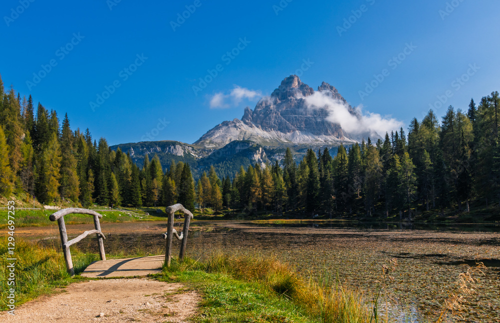 Tre Cime di Lavaredo during sunrise with warm golden light with small bridge and lake in the foreground