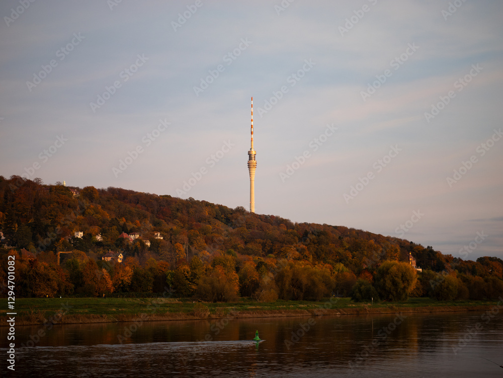 Obraz premium TV tower of Dresden, Germany illuminated by orange sunlight in the evening. Romantic landscape at the Elbe river in Wachwitz. Elbe valley at dusk during autumn season.
