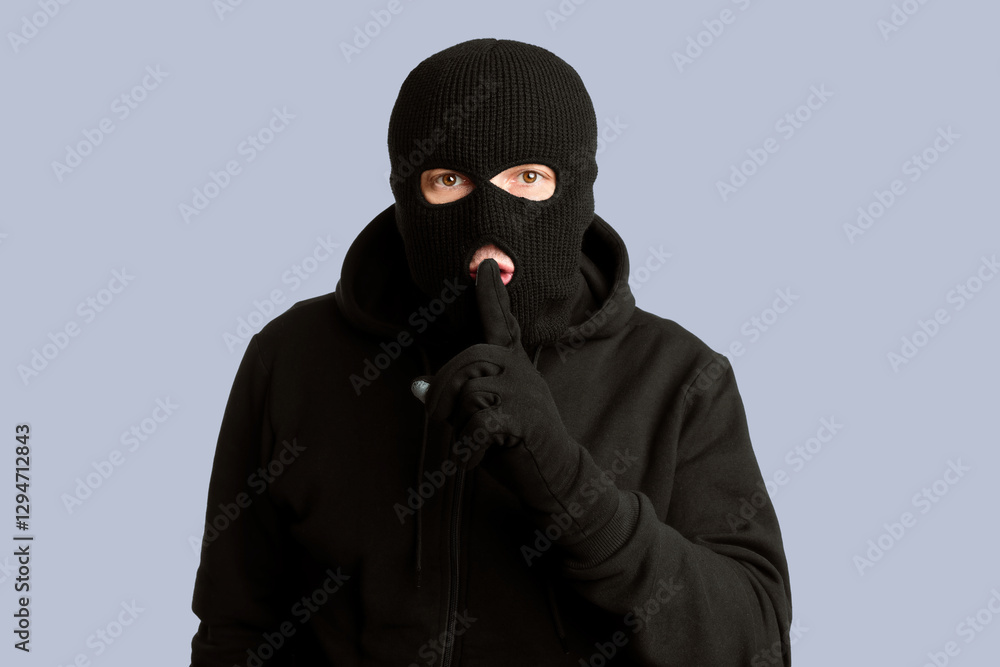 Keep Silence Concept. Portrait of thief in black balaclava holding fingers on lips, making hush sign, isolated on white wall Keep Silence Concept. Portrait of thief in black balaclava holding fingers on lips, making hush sign, isolated on white wall