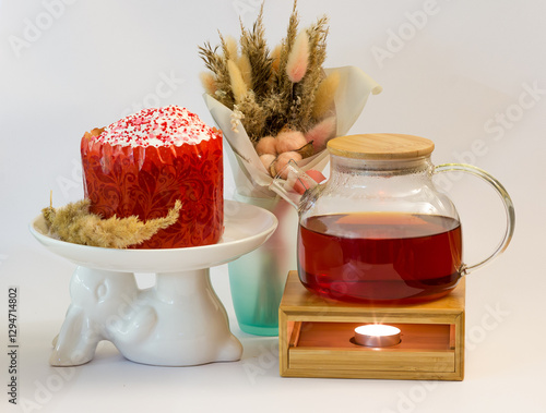 Easter cake on a plate in the shape of an Easter bunny with a teapot and a bouquet of dried flowers on a white background