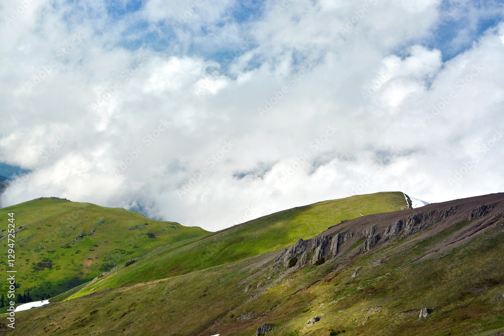 Fototapeta premium Cumulus clouds against green alpine meadows and mountains in the evening