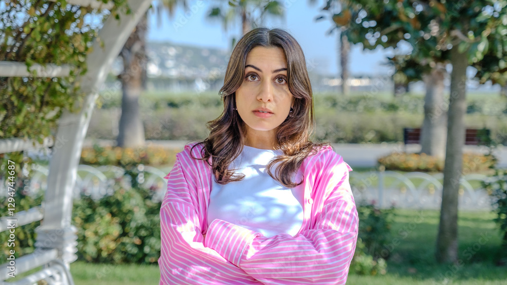 A young brunette businesswoman with a confused expression looking at the camera in a tree-filled park on a spring day A young brunette businesswoman with a confused expression looking at the camera in a tree-filled park on a spring day