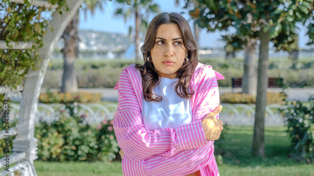 A young, beautiful, brunette business woman in the park looks at the camera with a facial expression that clearly shows that she is cold A young, beautiful, brunette business woman in the park looks at the camera with a facial expression that clearly shows that she is cold