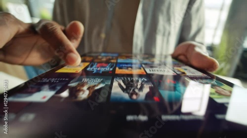 Europe- March 17 2022: Close-up footage of male fingers touching screen of digital tablet. Unrecognizable African man in casual outfit using streaming platform, browsing app to find show to watch on