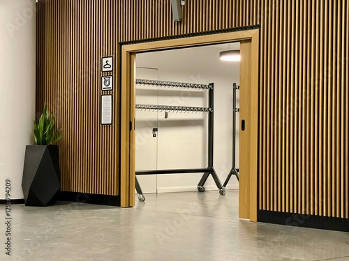 Modern cloakroom entrance with wooden panel walls and a minimalist design. The space features rolling coat racks, a sliding wooden door, and a geometric plant pot for decoration
