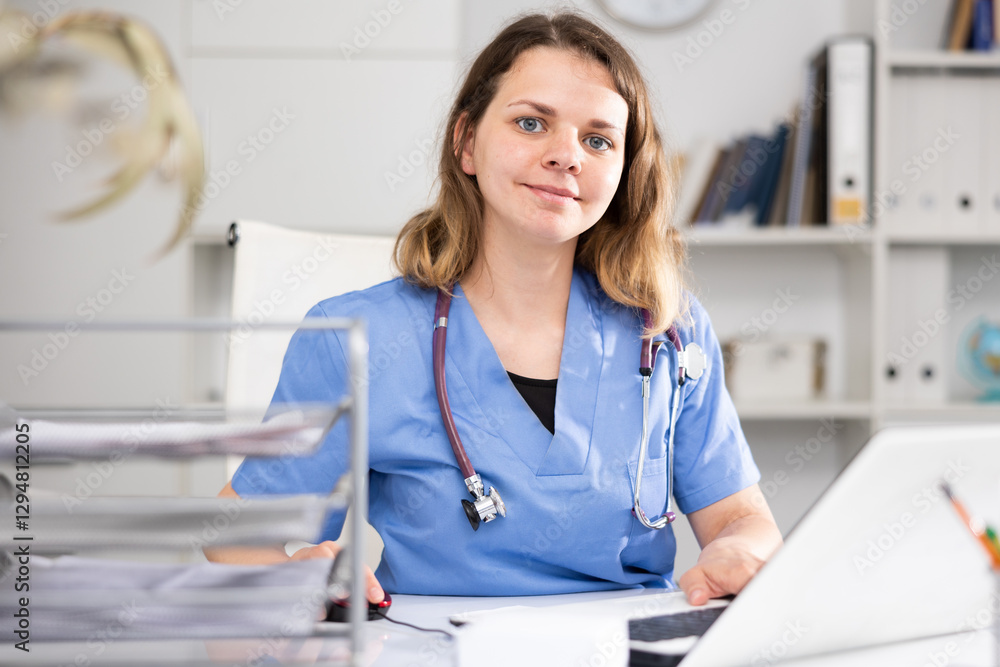 Positive woman doctor sitting at workplace with computer in her office Positive woman doctor sitting at workplace with computer in her office