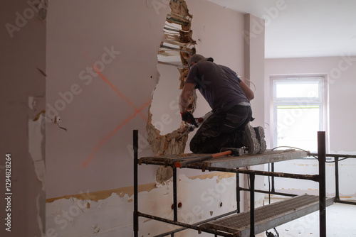 Obraz na płótnie A construction worker on scaffolding demolishes a wall in a building with a hammer drill. w salonie