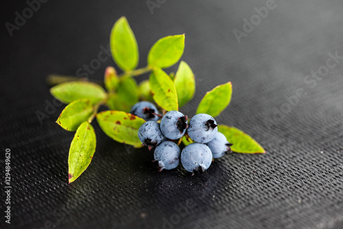 Fresh Maine blueberries on a dark surface with green leaves in a naturallighting photo