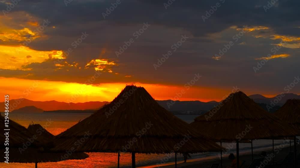 Breathtaking sunset behind beach umbrellas. Tourists enjoying the beach bask in the last rays of sunlight as the sun sets behind straw umbrellas. A vibrant sky transitions through shades of orange. Breathtaking sunset behind beach umbrellas. Tourists enjoying the beach bask in the last rays of sunlight as the sun sets behind straw umbrellas. A vibrant sky transitions through shades of orange.