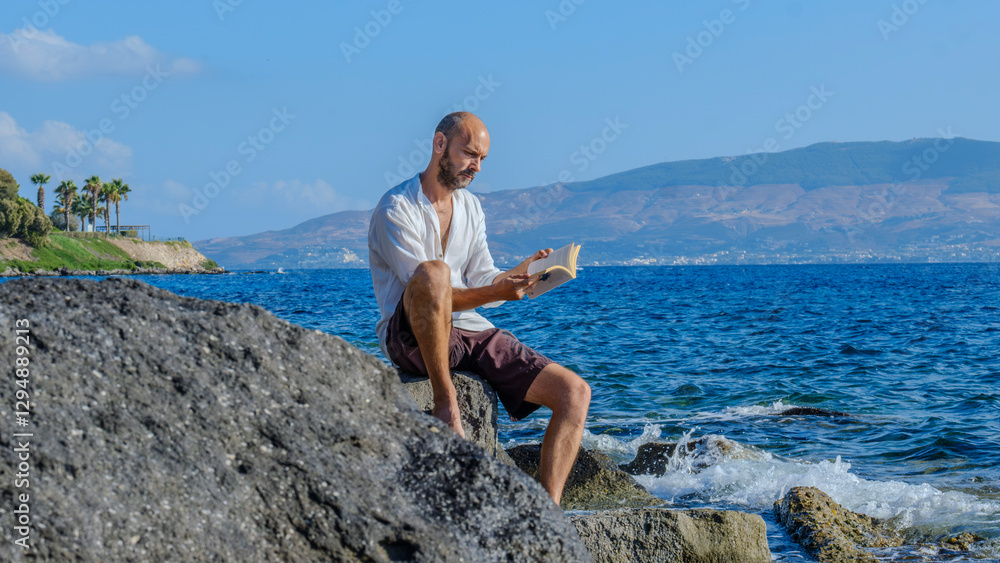 A middle-aged charismatic man, wearing a white shirt, is sitting on the rocks by the seaside on a sunny summer day, reading a book and enjoying the sun while on vacation A middle-aged charismatic man, wearing a white shirt, is sitting on the rocks by the seaside on a sunny summer day, reading a book and enjoying the sun while on vacation