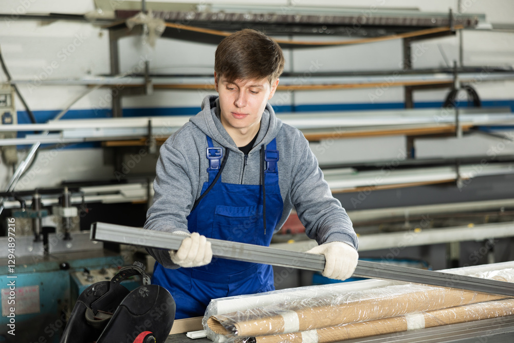 Young guy worker in uniform taking steel profile pipe in warehouse Young guy worker in uniform taking steel profile pipe in warehouse