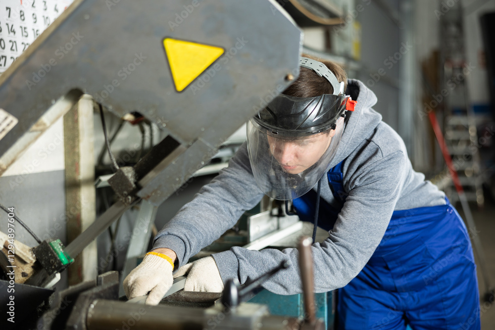 Young guy worker in safety helmet puts steel part on machine in factory