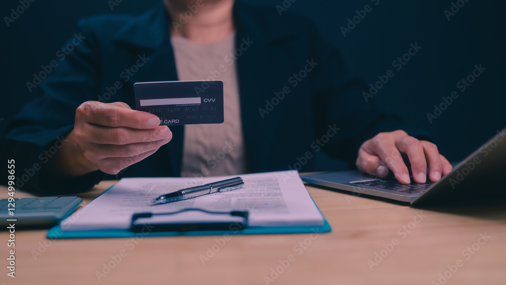 Fototapeta premium A woman is holding a credit card and typing on a laptop. Concept of financial responsibility and organization