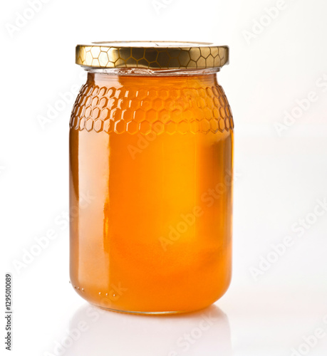 Freshly harvested honey in a clear jar with a golden lid on a white background