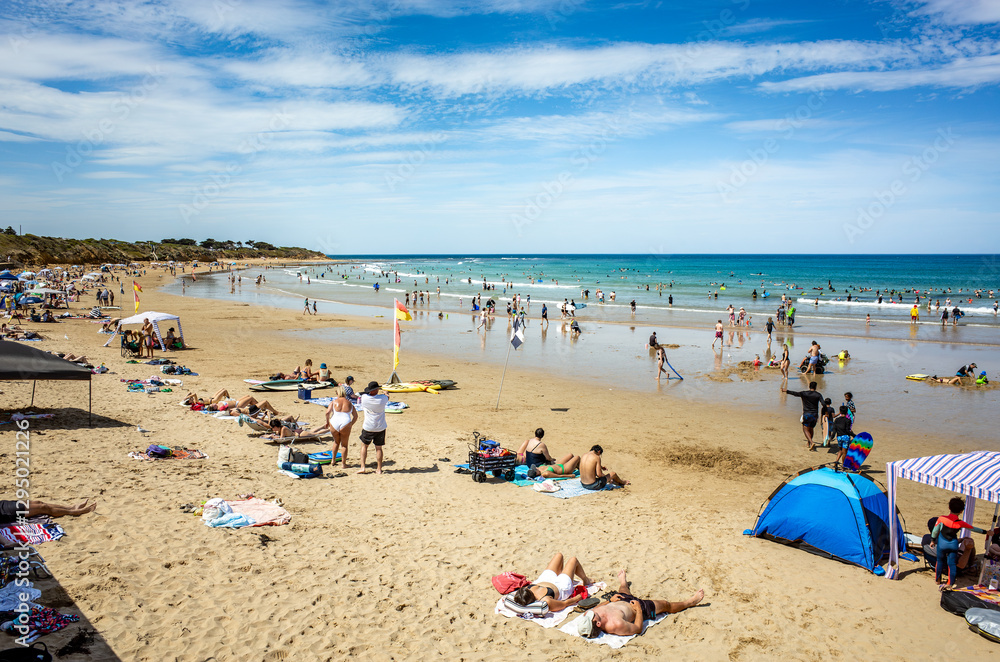 Summer scene at Torquay Surf Beach, Australia, with beachgoers sunbathing, swimming, and enjoying the coastal waters. The sand, blue ocean, and scattered tents create a lively and holiday atmosphere Summer scene at Torquay Surf Beach, Australia, with beachgoers sunbathing, swimming, and enjoying the coastal waters. The sand, blue ocean, and scattered tents create a lively and holiday atmosphere