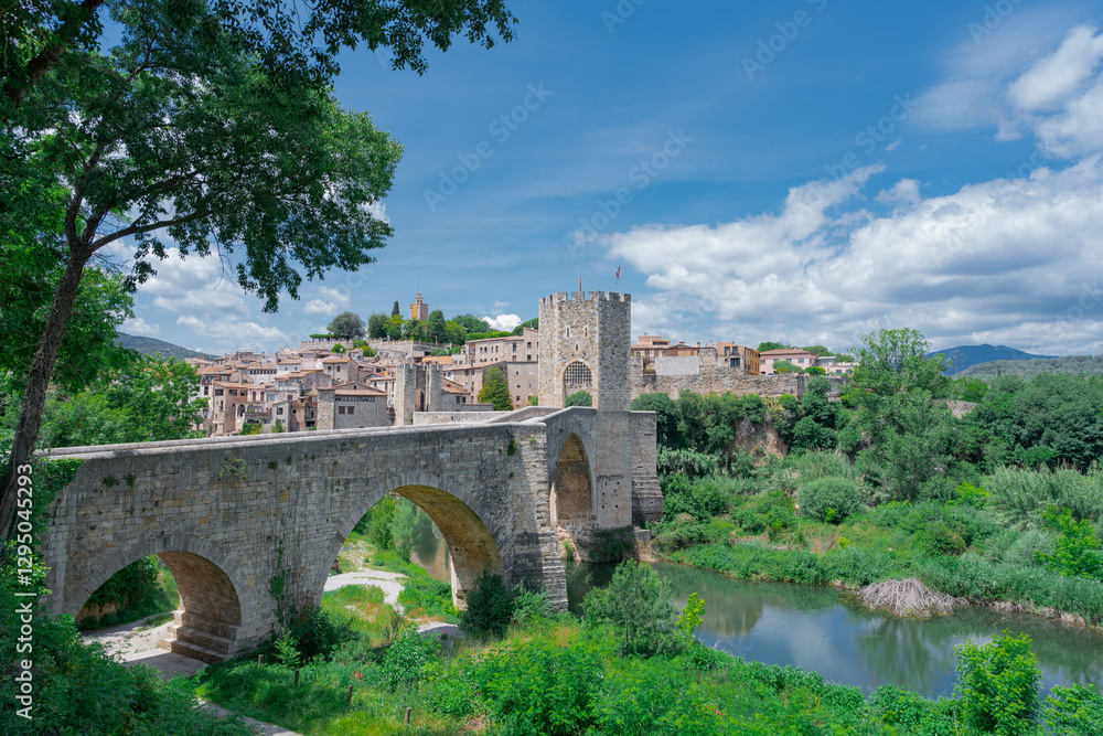 Puente medieval sobre un rio con vegetación, un dia soleado con cielo azul y nubes. Desde Besalú, Gerona, Cataluña, España. Puente medieval sobre un rio con vegetación, un dia soleado con cielo azul y nubes. Desde Besalú, Gerona, Cataluña, España.