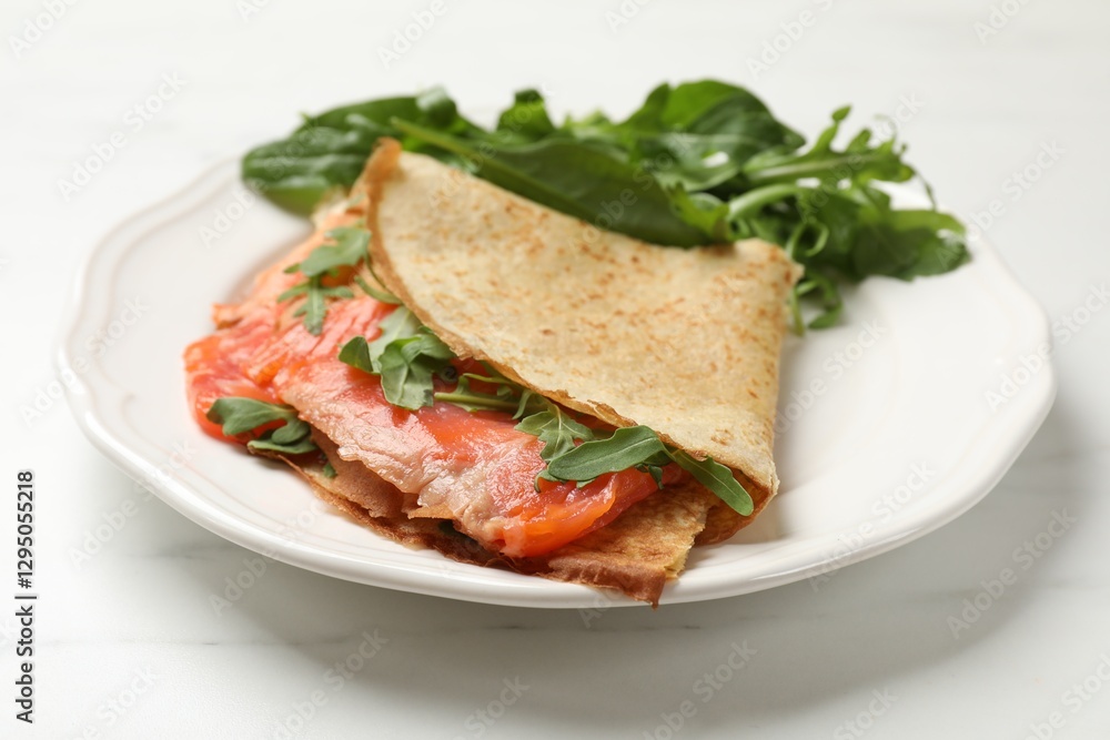 Delicious crepes with salmon and arugula on white table, closeup Delicious crepes with salmon and arugula on white table, closeup