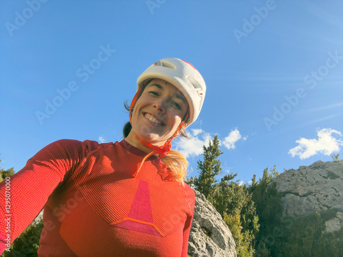 A woman wearing a red shirt and helmet is smiling at the camera. Concept of adventure and excitement, as the woman is likely preparing for a mountain climb or other outdoor activity photo