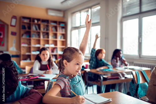Young Caucasian girl raising her hand for the teacher while at the elementary school classroom