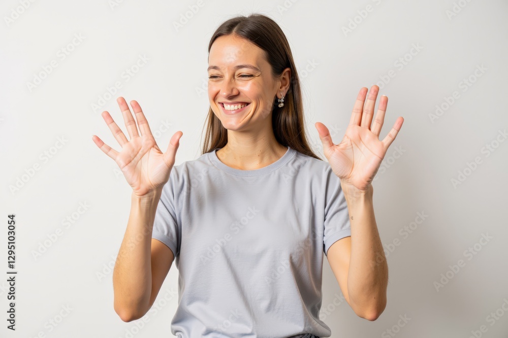 Smiling Young Caucasian Woman in Gray Shirt Gesturing with Happy Hand Signals, Communicating Joy and Positivity Against a Neutral Background Smiling Young Caucasian Woman in Gray Shirt Gesturing with Happy Hand Signals, Communicating Joy and Positivity Against a Neutral Background