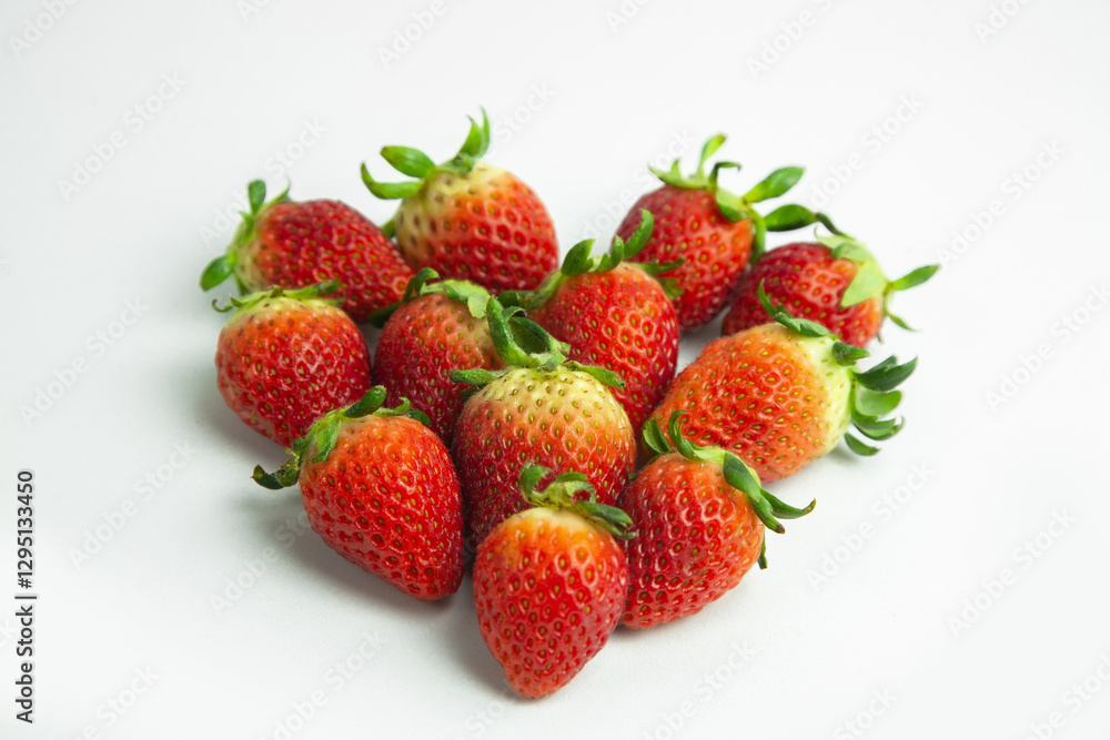strawberries are arranged in a heart shape on a white background. The berries are red with green stems, some showing a transition to lighter, unripe areas. The image is a top-down view strawberries are arranged in a heart shape on a white background. The berries are red with green stems, some showing a transition to lighter, unripe areas. The image is a top-down view