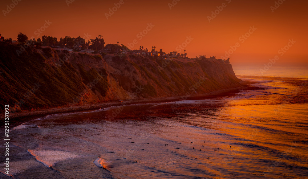 Bluff Cove, Palos Verdes Estates, surfers below wait for the next wave as the sky gives off dramatic hues of red and orange